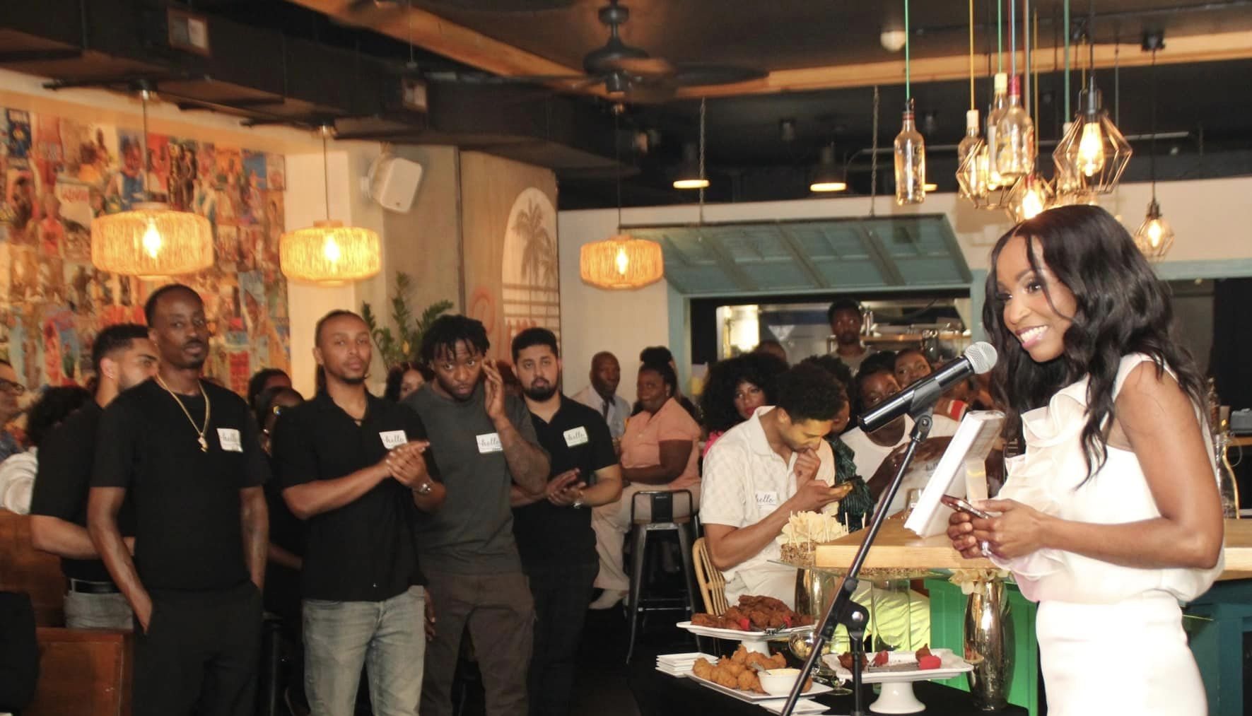 Melane Mullings speaking at a microphone to a room of guests