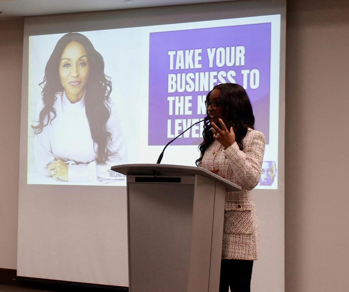 Melane Mullings speaking at a podium in front of a presentation screen