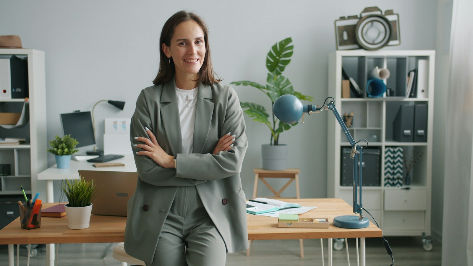 A smiling businesswoman in a grey suit standing with arms crossed in her office