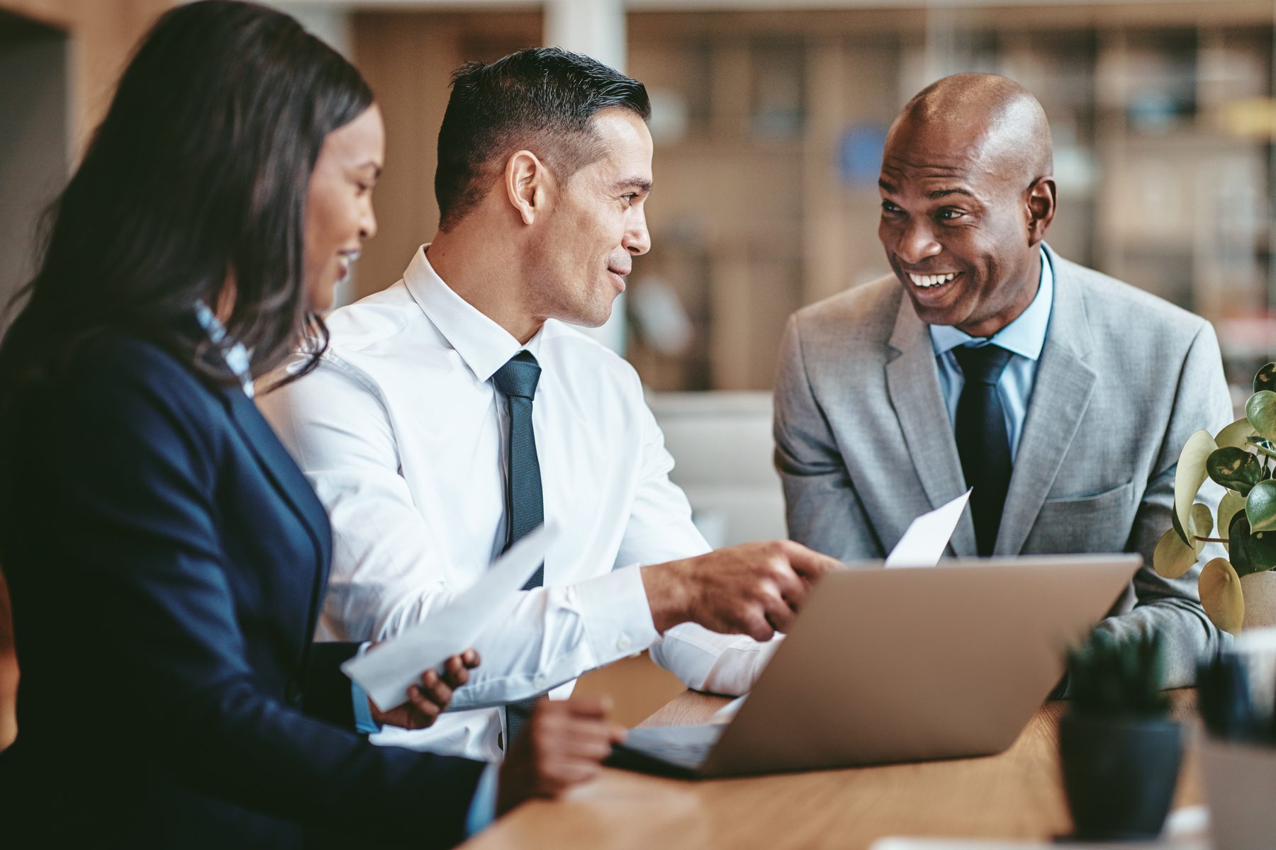 Three colleagues in business attire smiling during a meeting around a laptop